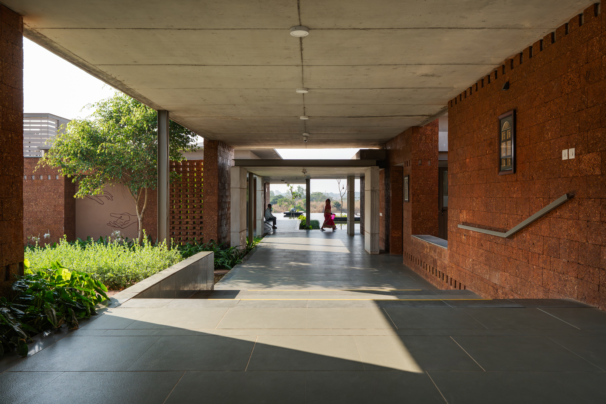 Long covered colonnade with concrete ceiling and a red laterite wall on one side