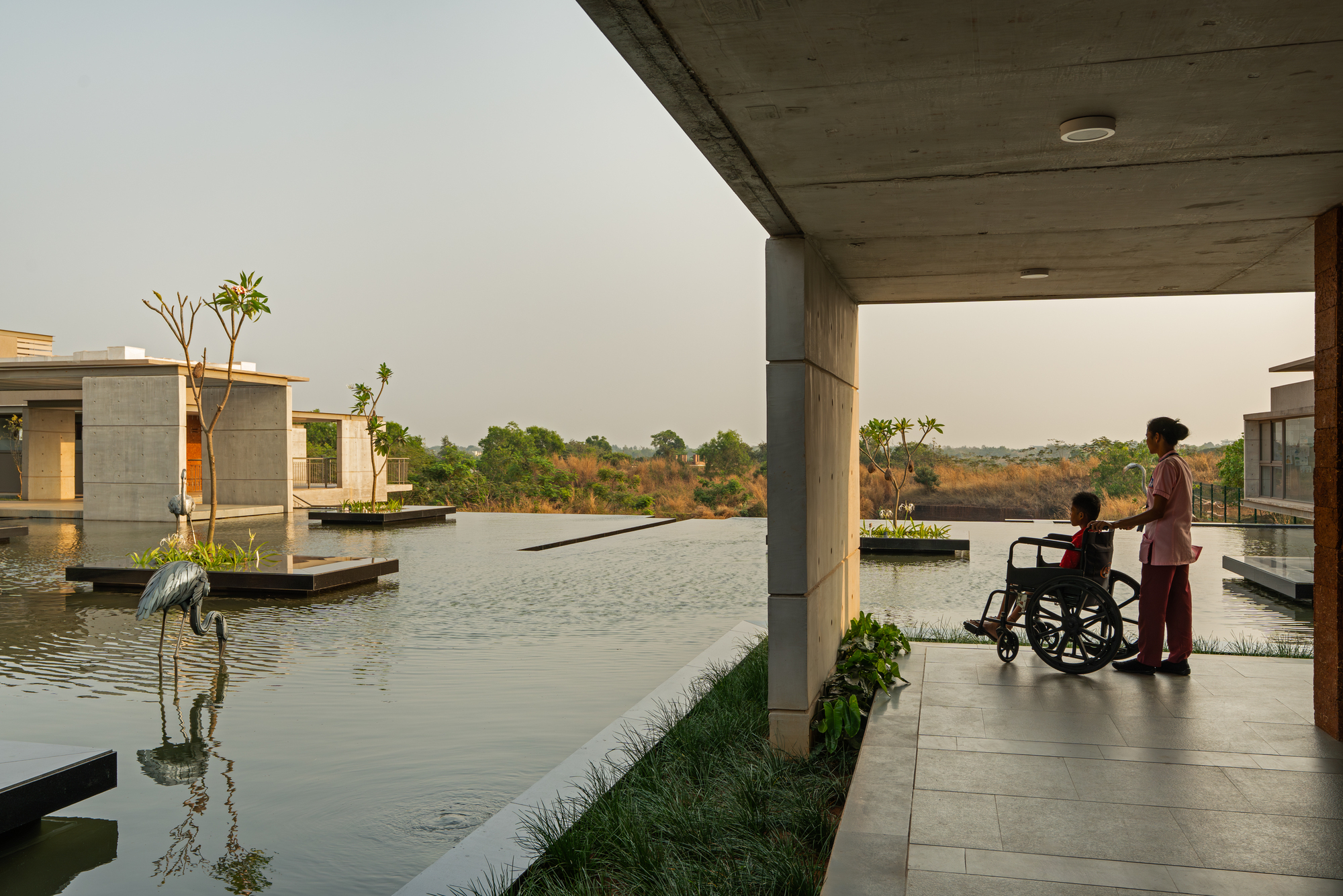 A patient in a wheelchair with an attendant looking across the reflecting pool from a covered walkway
