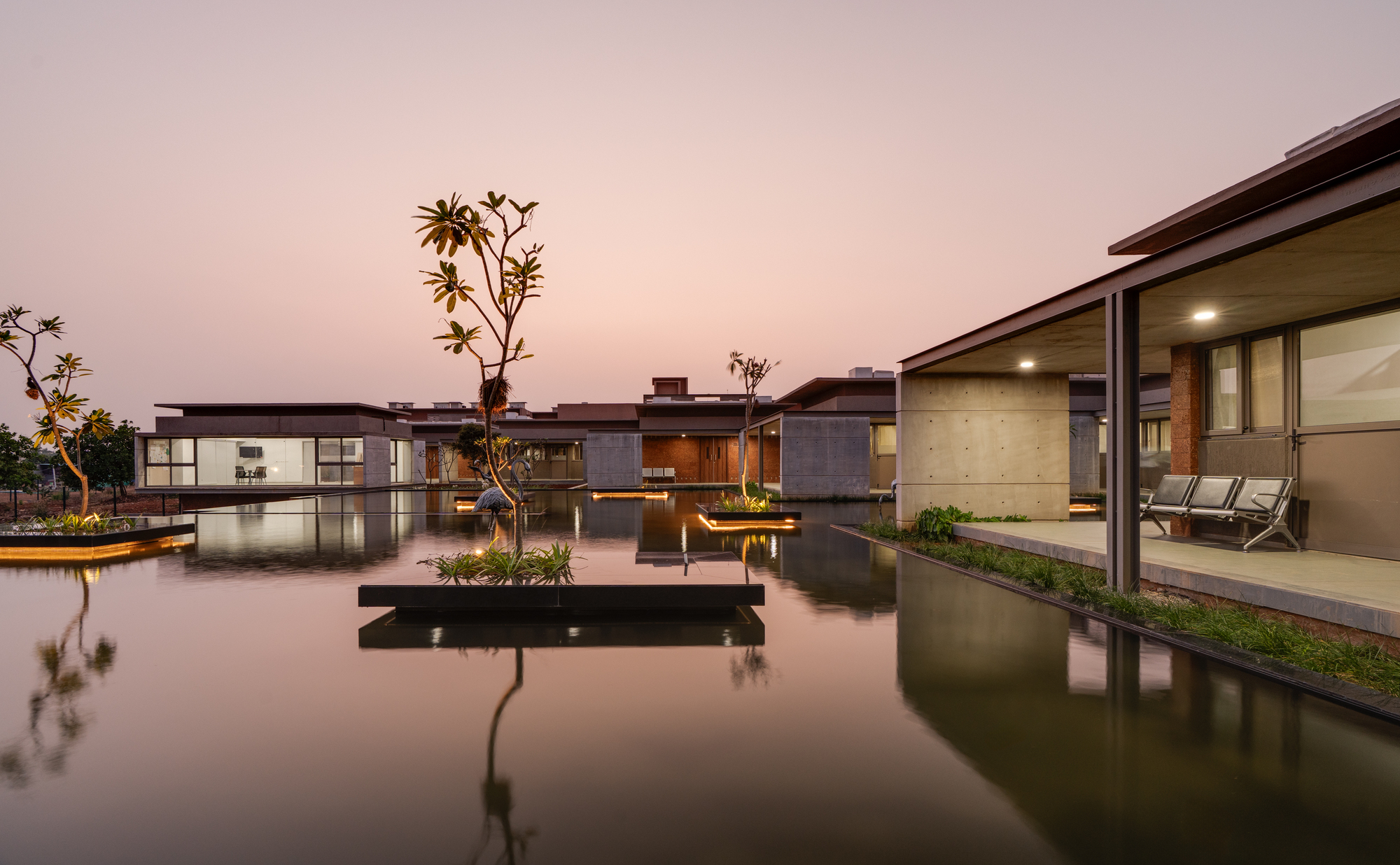 Dusk view of the ward complex mirrored in a calm reflecting pool with floating planters