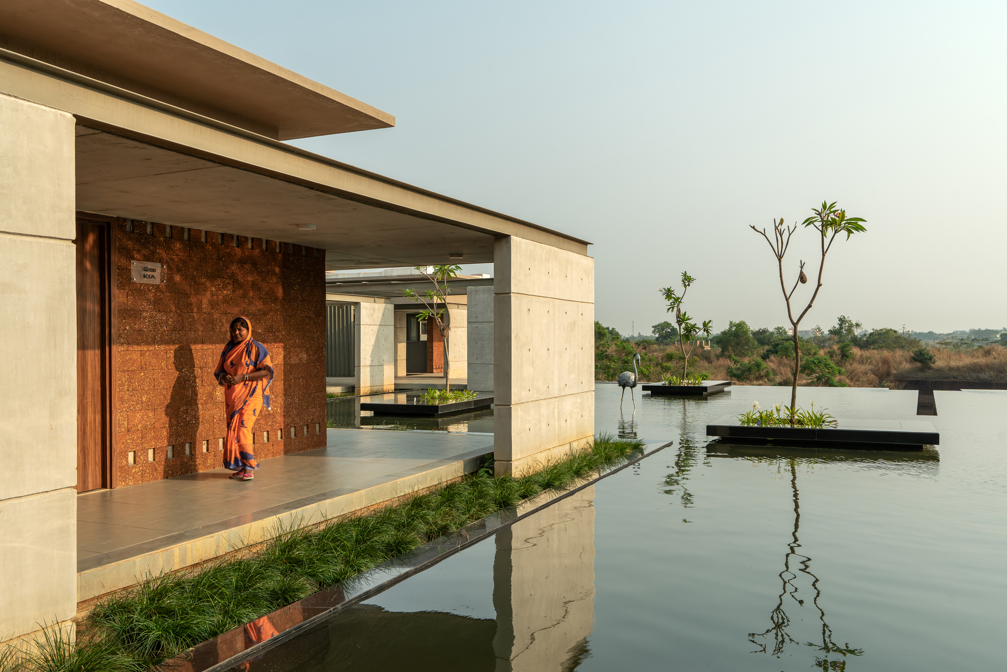Open veranda facing a still reflecting pool with a sari-clad figure standing in shadow