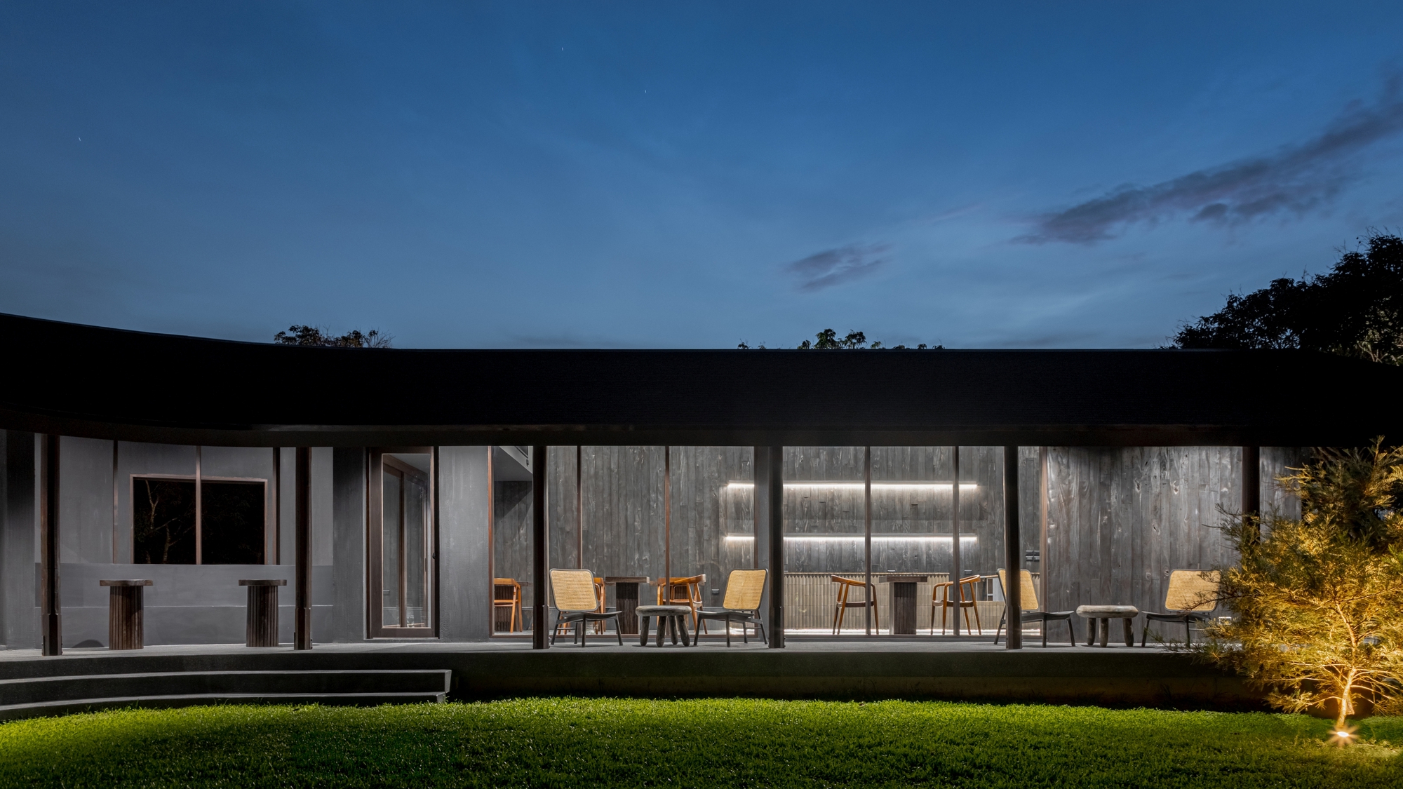 Night elevation of the glazed dining pavilion with timber chairs on the terrace
