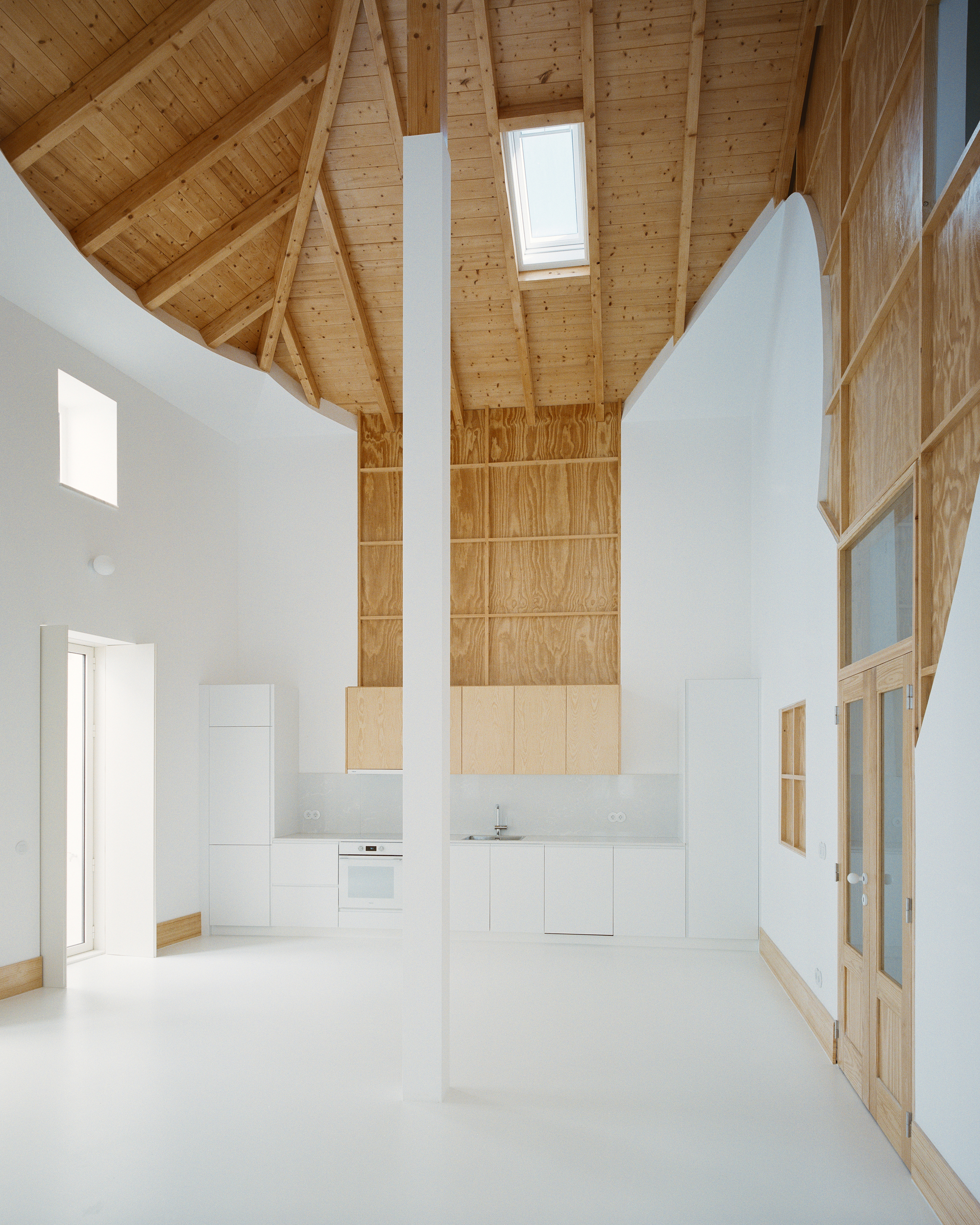 Open kitchen below the pine ceiling with a tall plywood feature wall and central pillar