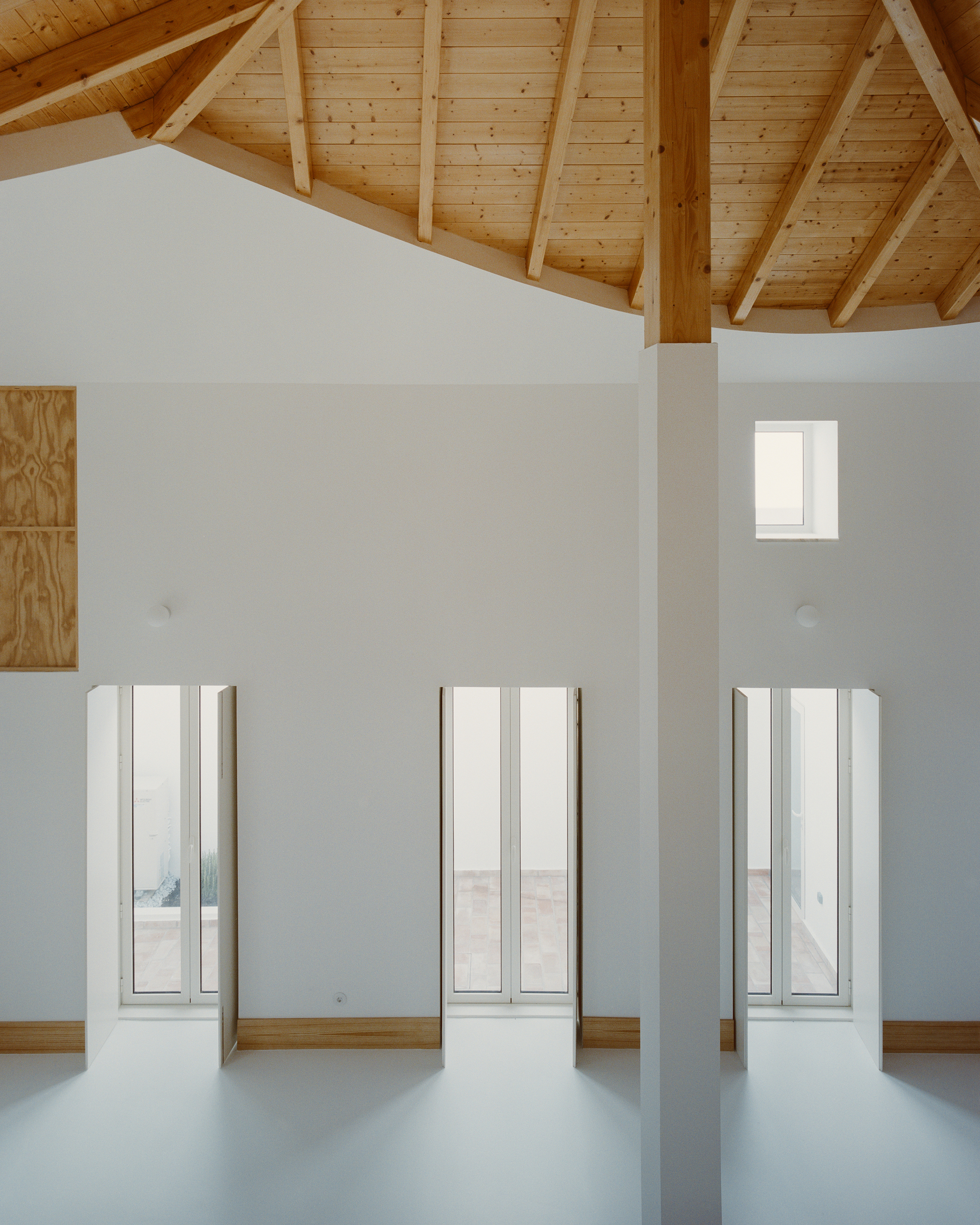 Three full-height window slots on a white wall under the exposed pine roof structure