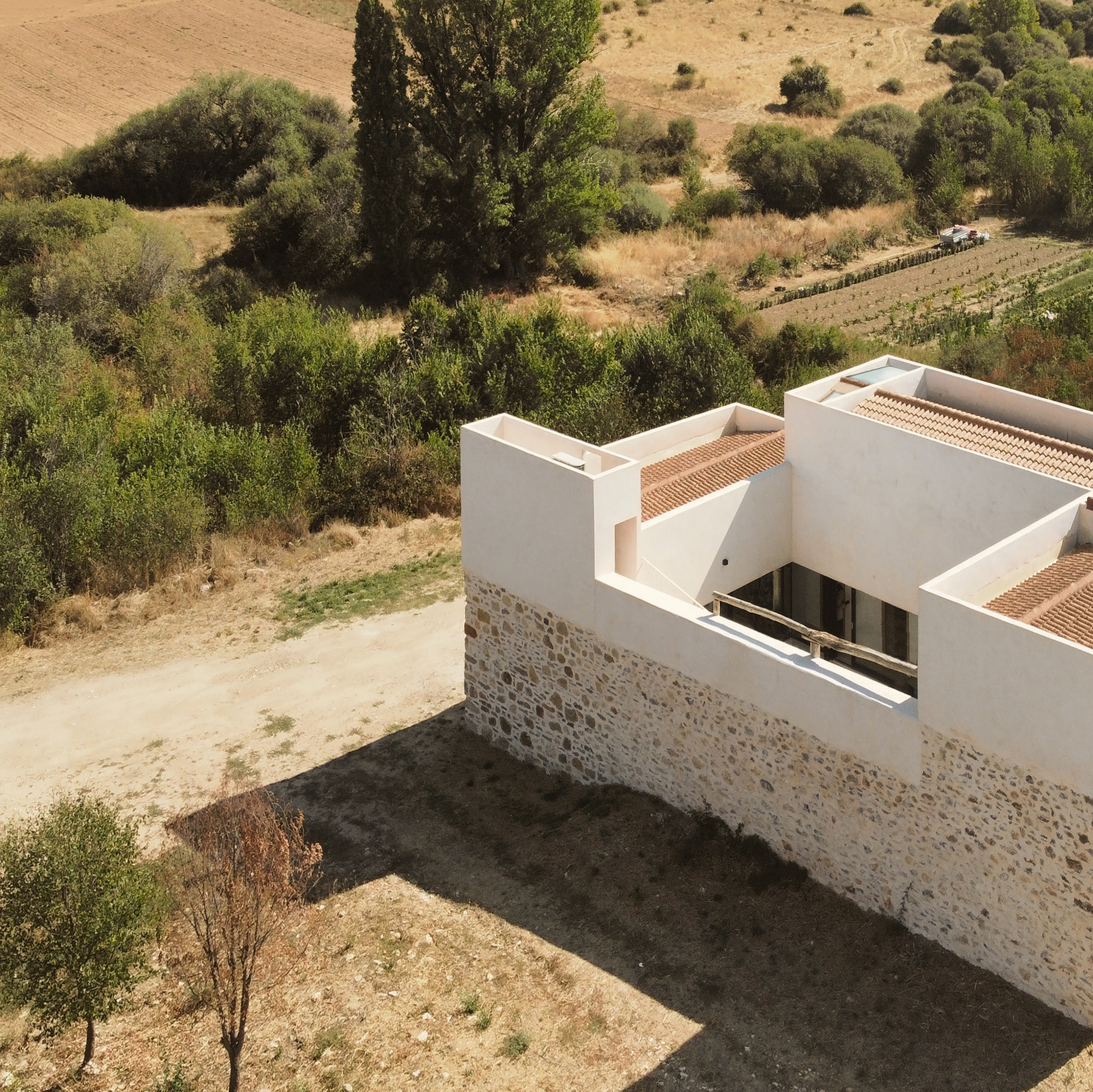 Drone shot of the new white volume rising above the original stone walls toward the surrounding fields