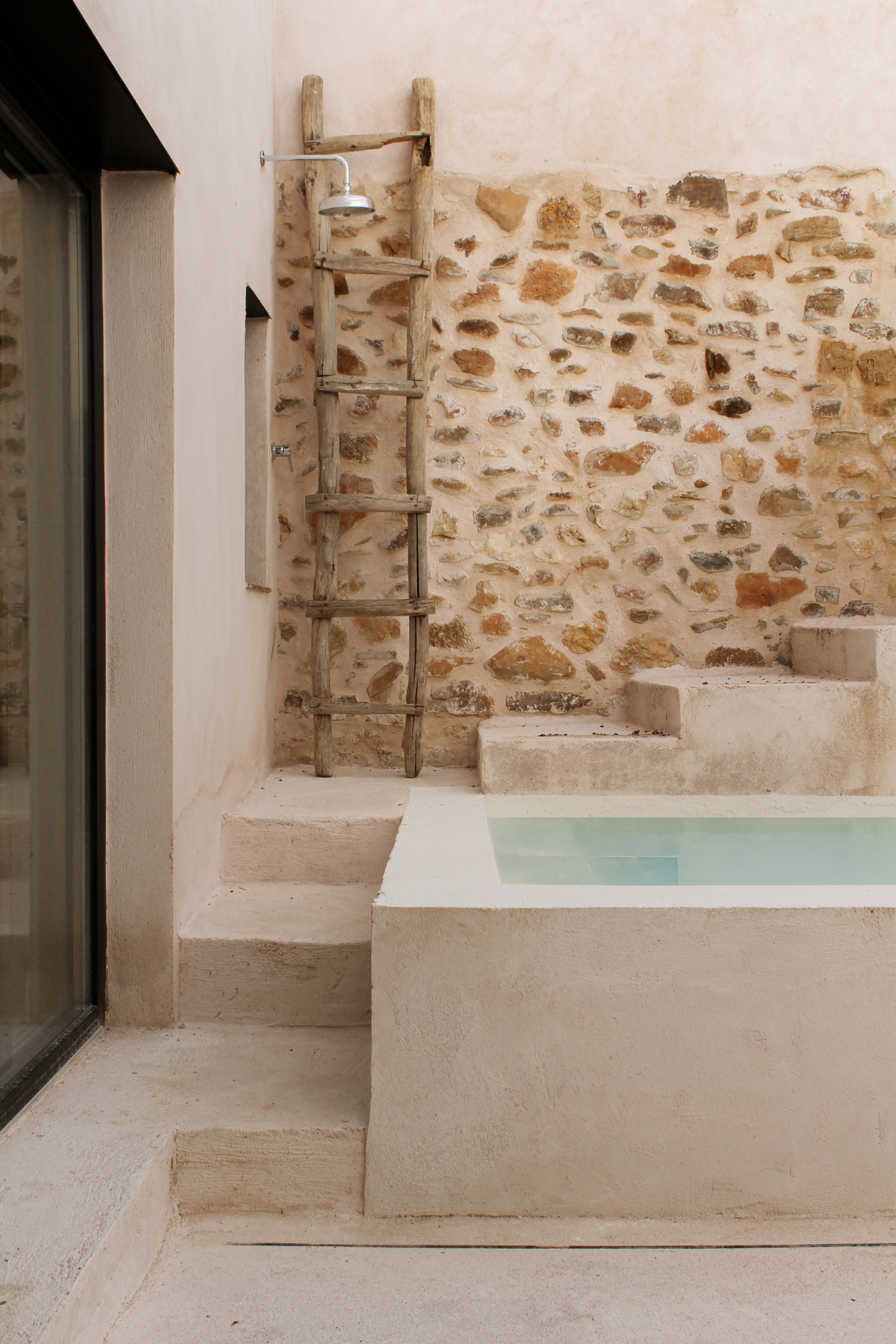 Detail of the courtyard pool with an outdoor shower against the stone wall