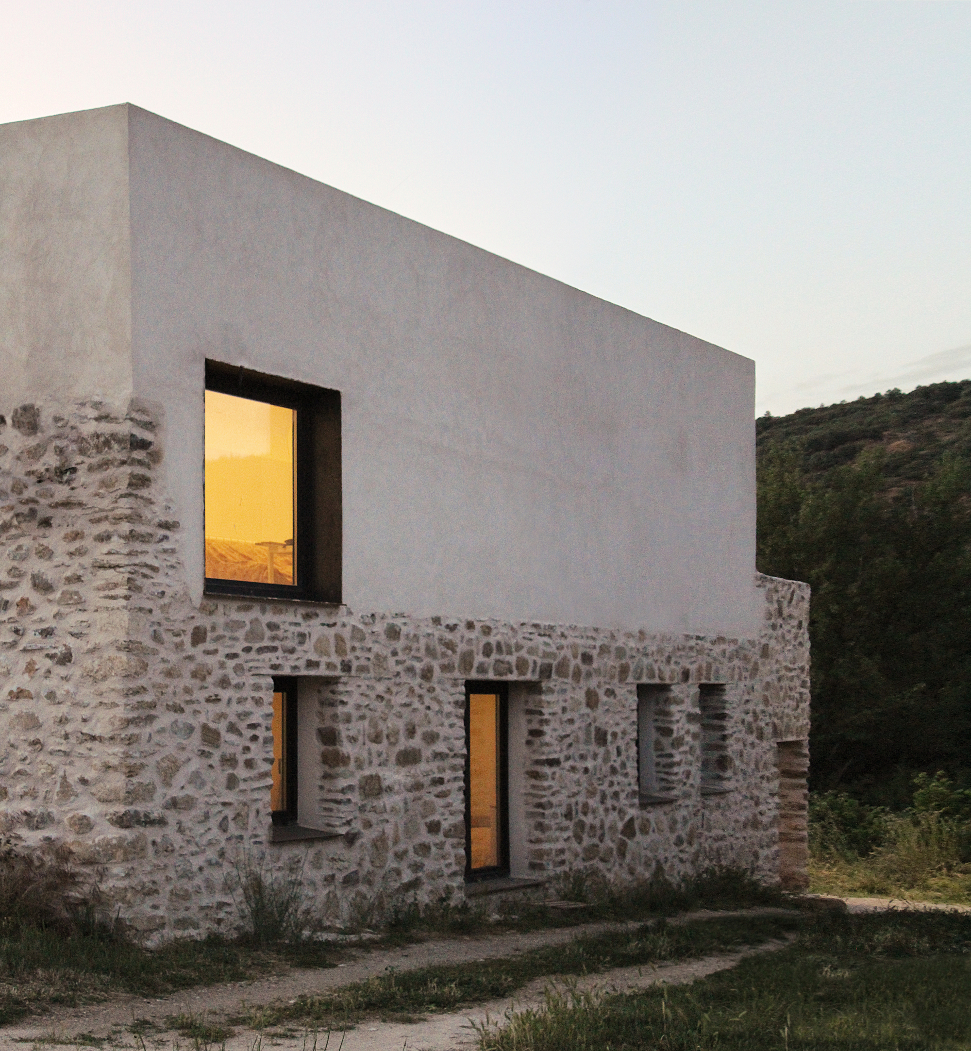 Dusk elevation showing the house lit from inside with the white volume above the stone base