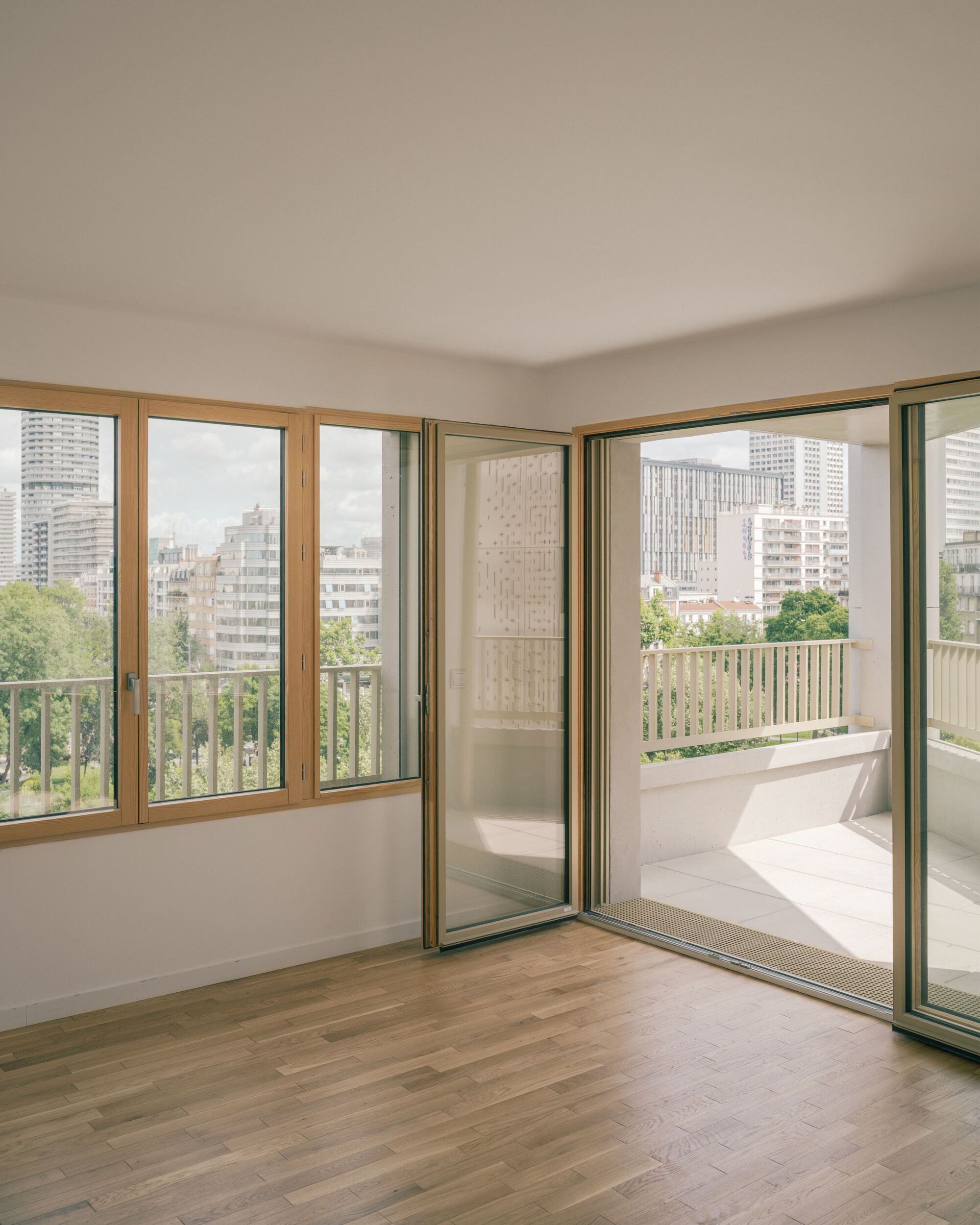 Empty family flat with timber-framed corner windows opening onto a long balcony with views over Paris