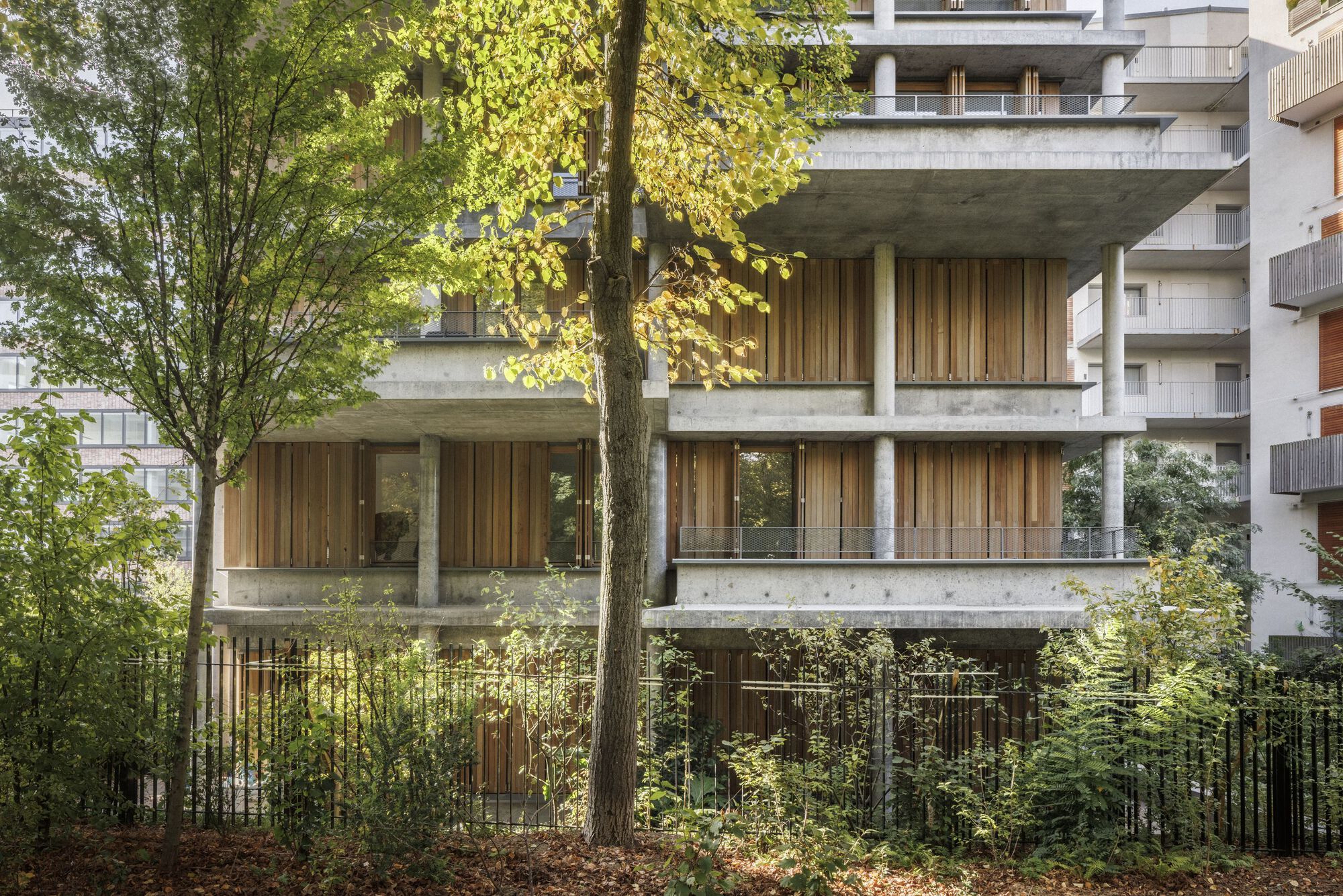 Concrete frame and timber-louvered facade of the social housing seen from the trees