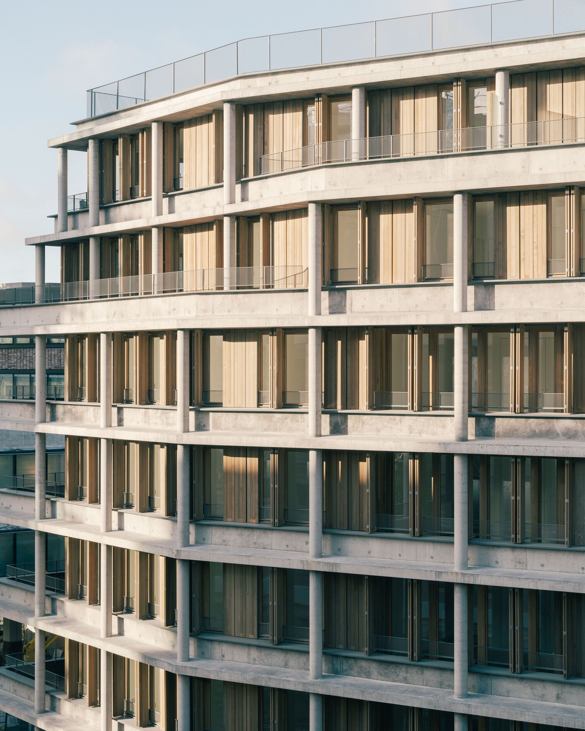 Curved corner of the family-flat block with concrete columns and timber screens at sunset