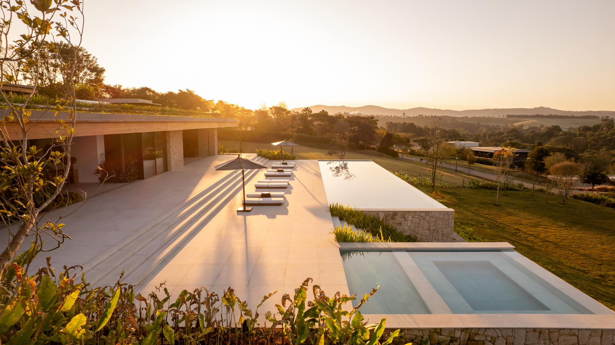 Golden hour view along the terrace edge with the reflecting pool and the distant hills of Bragança Paulista