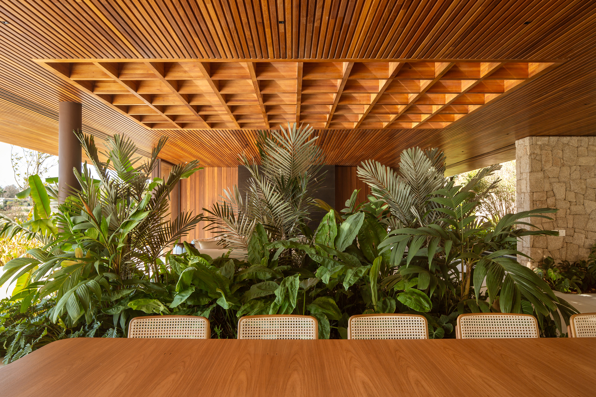 Dining area under a deep timber coffered ceiling with a dense planted bed behind the table