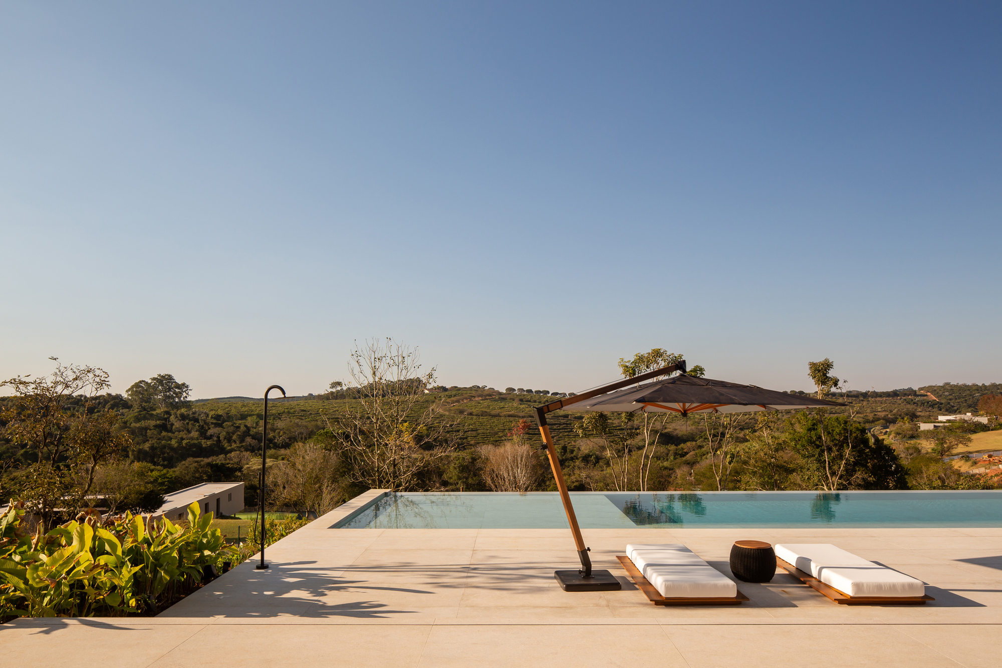 Pool deck with a single umbrella and two white sun loungers looking out toward the hills
