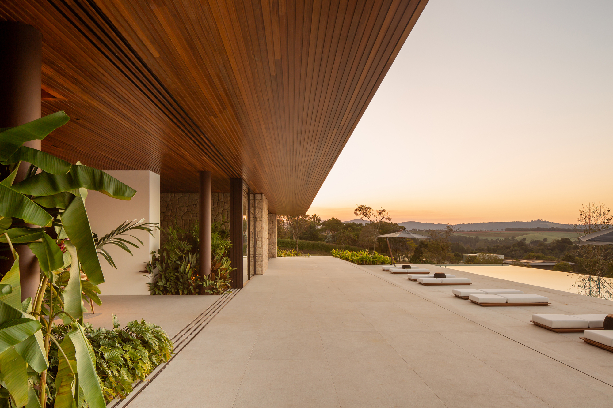 Covered veranda at sunset looking along the pool deck with lounge cushions and the timber slatted ceiling above