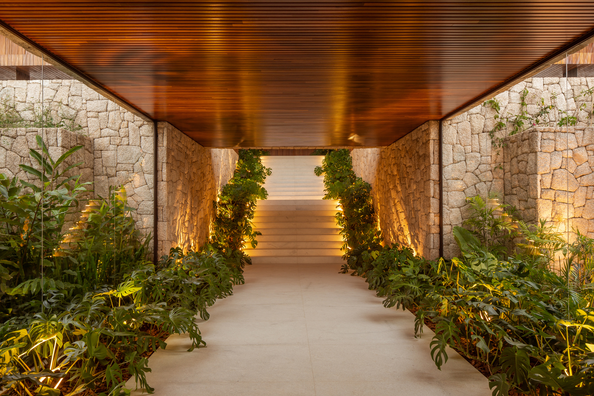 Narrow entry passage between stone walls leading into the house with integrated planting along both sides