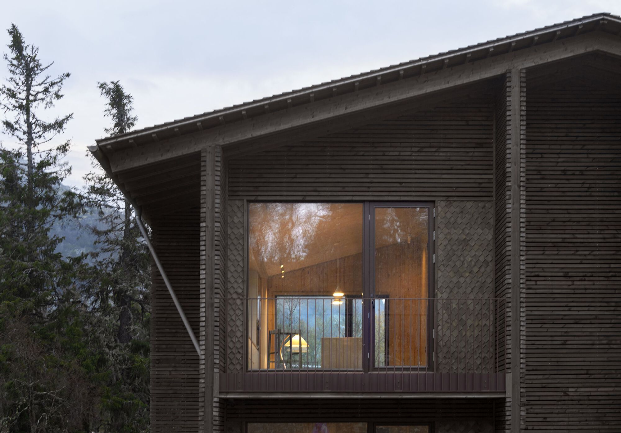 Upper-floor panoramic window and gabled roof against the treeline